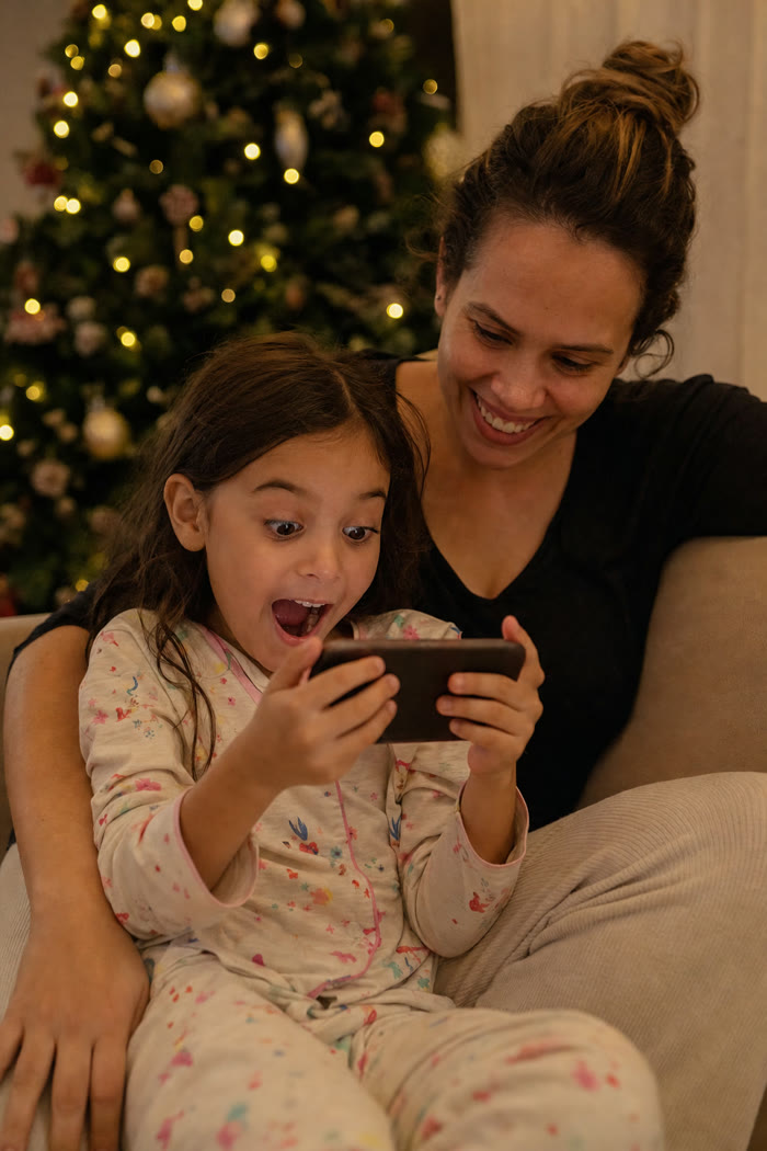 Menina vendo o vídeo do Papai Noel com a mãe, surpresa e feliz